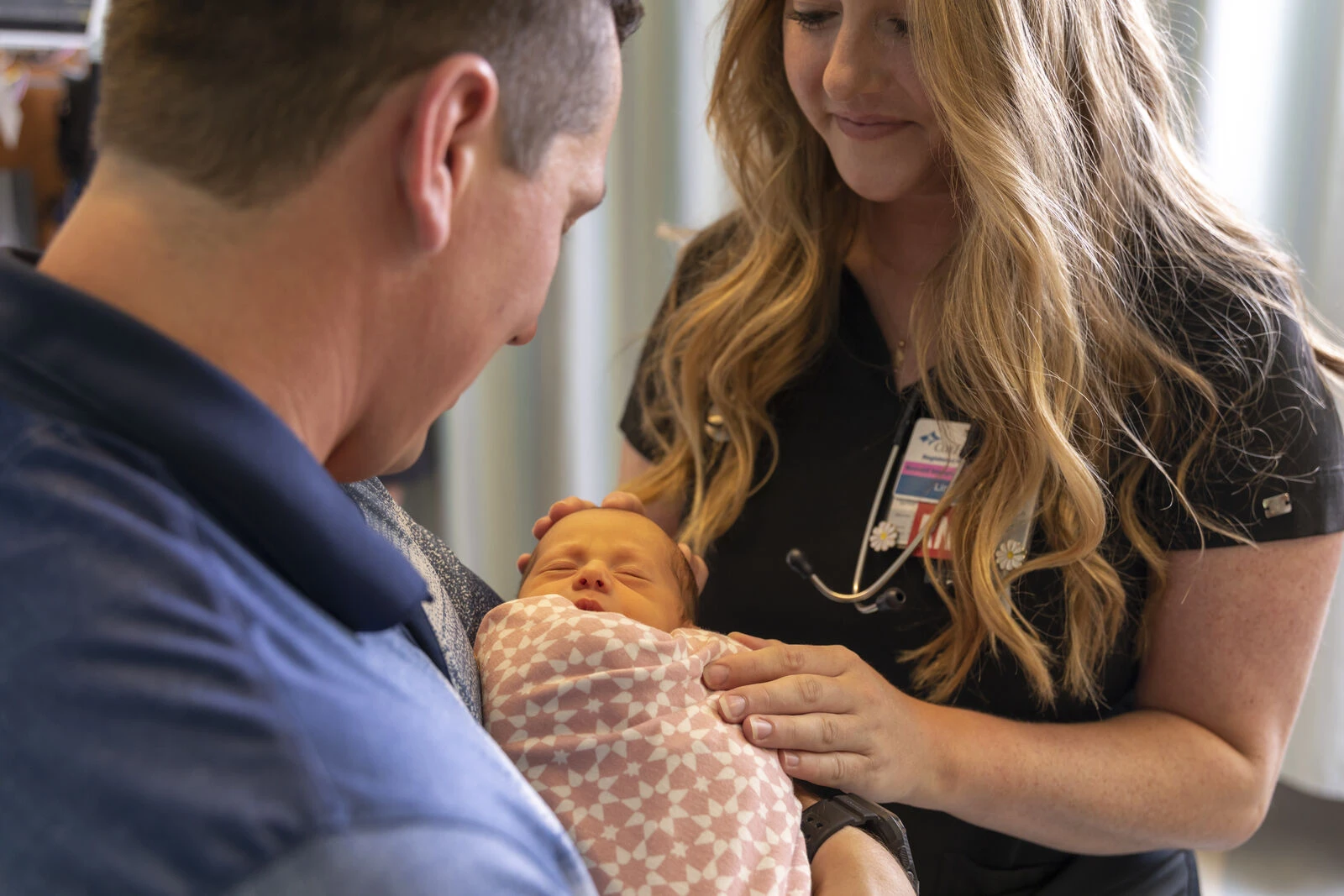 A healthcare worker helping a parent hold a newborn baby.